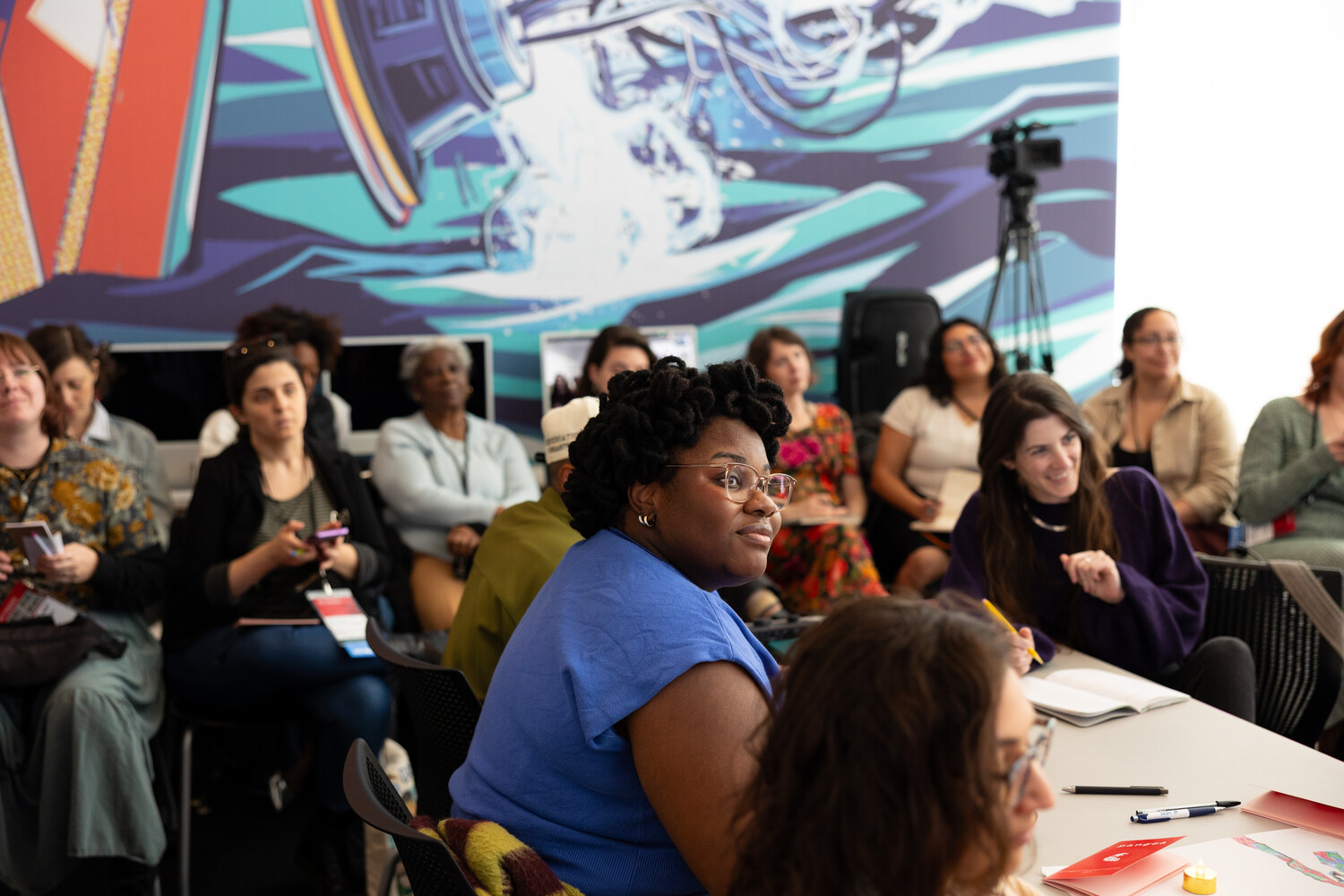 Workshop attendees listening in front of a mural